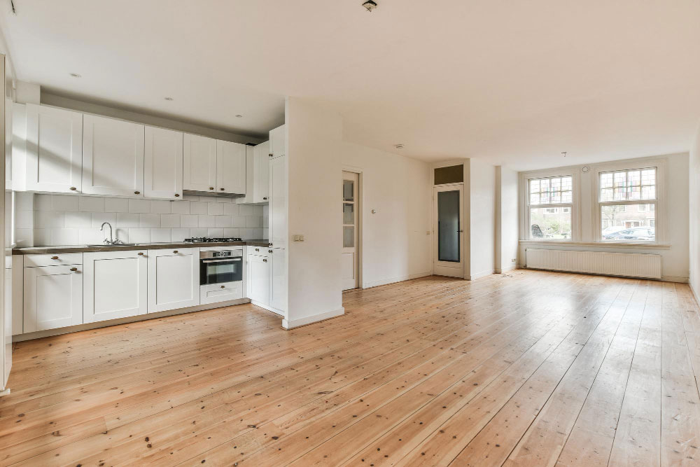 Jak pronajímat byt: Prázdný obývá a kuchyňský kout se světlými bílými zdmi a dřevěnou béžovou podlahou.